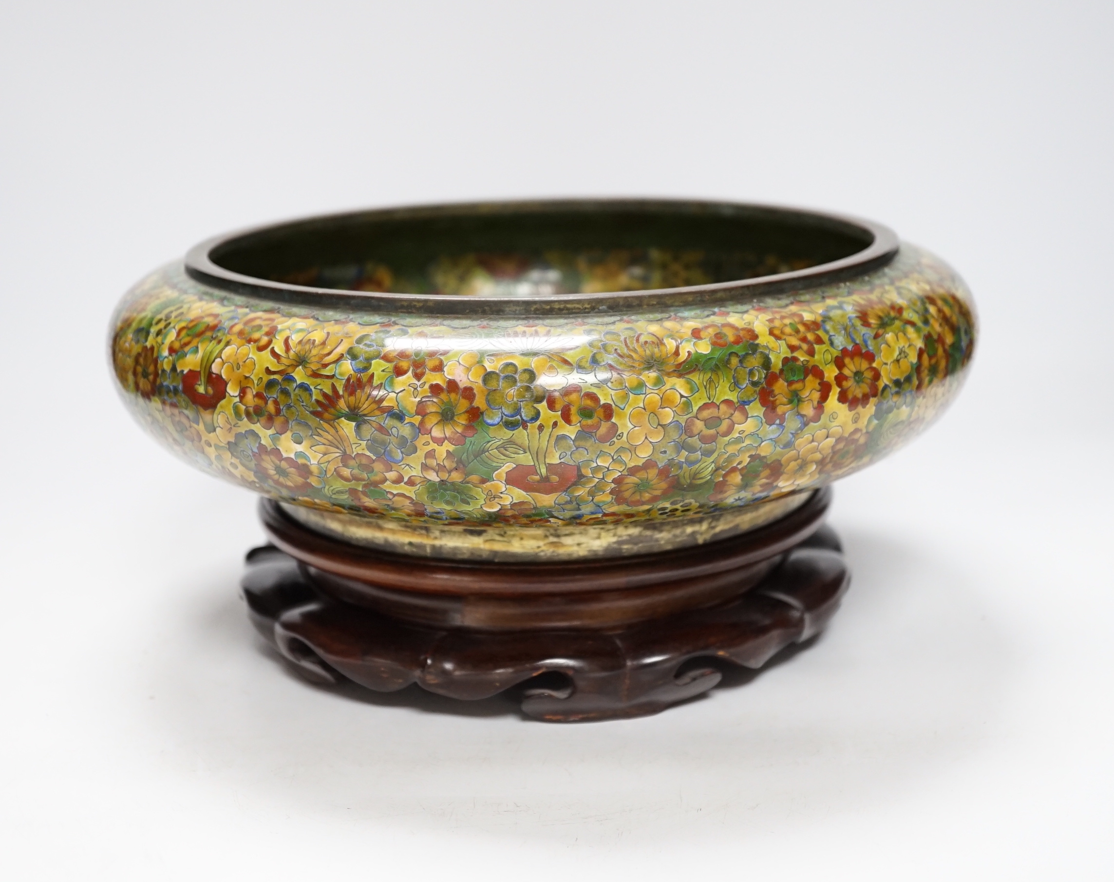 A Chinese circular cloisonné enamel bowl decorated with multi-coloured flowerheads on wooden stand, 30cm diameter